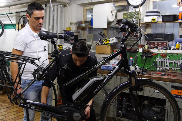 Ein Ausbilder leitet einen Auszubildenden an, der ein Fahrrad repariert.