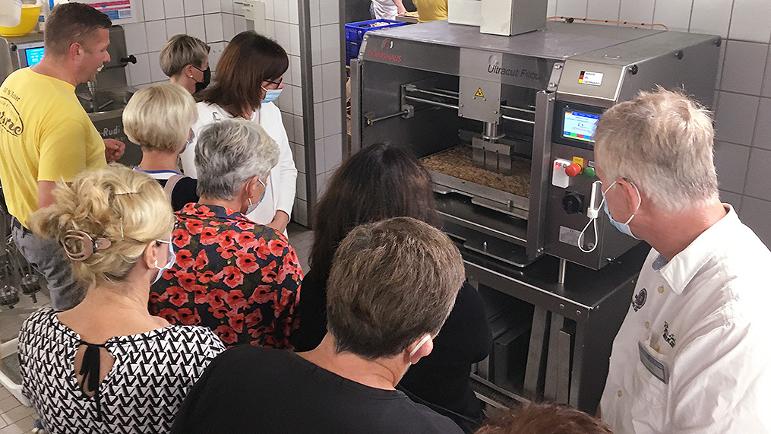 Menschengruppe betrachtet eine digital gesteuerte Kuchen-Schneidemaschine in einer Bäckerei