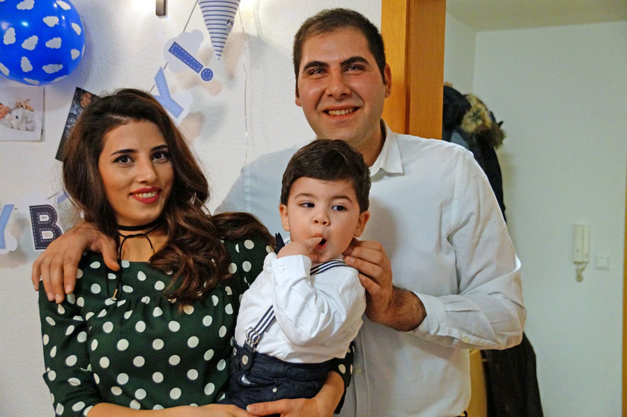 Eine junge Familie mit ihrem Sohn. Die Frau trägt eine schwarze Bluse mit weißen Punkten, Mann und Sohn ein weißes Hemd.